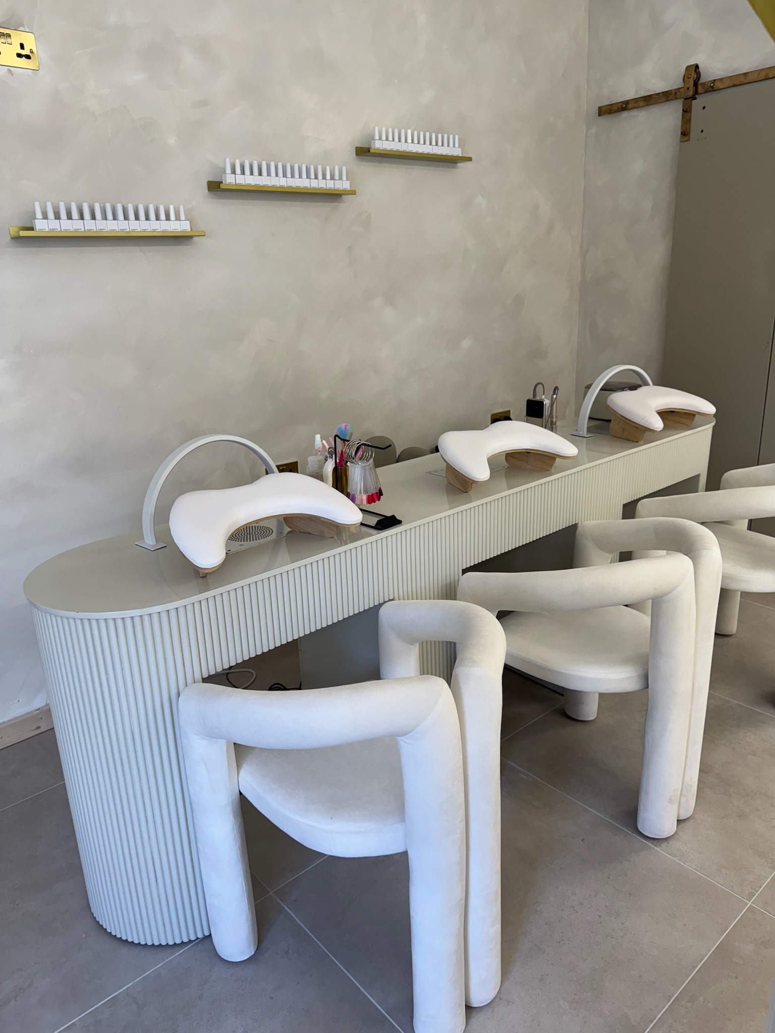 Manicure station with fluted desk, modern chairs, and nail polish display shelves