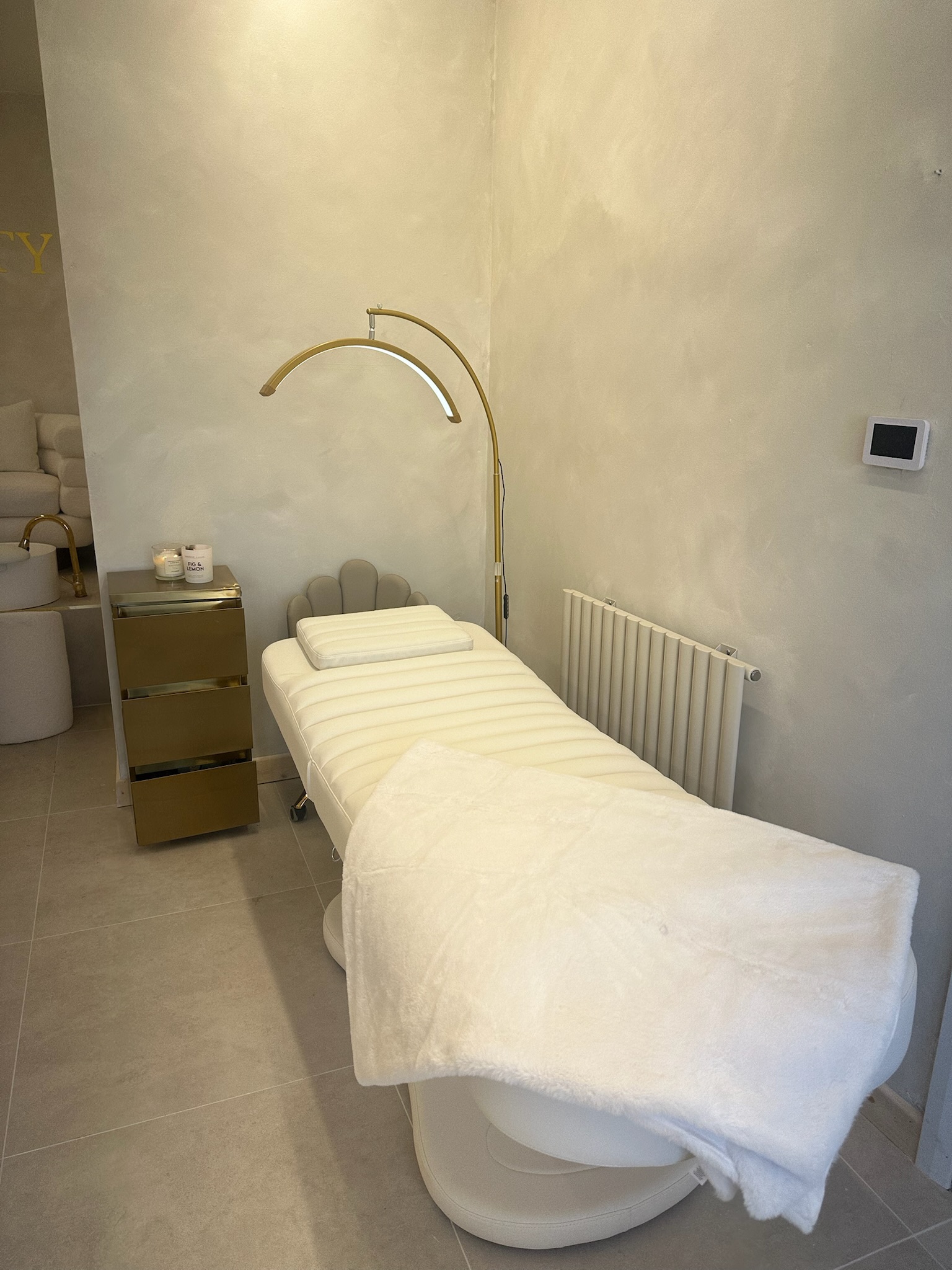 Treatment room with white bed, gold arch lamp, and calming interior design