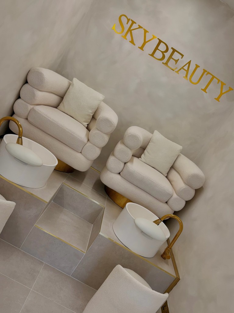 Pedicure station with plush white chairs, gold basins, and SkyBeauty wall branding