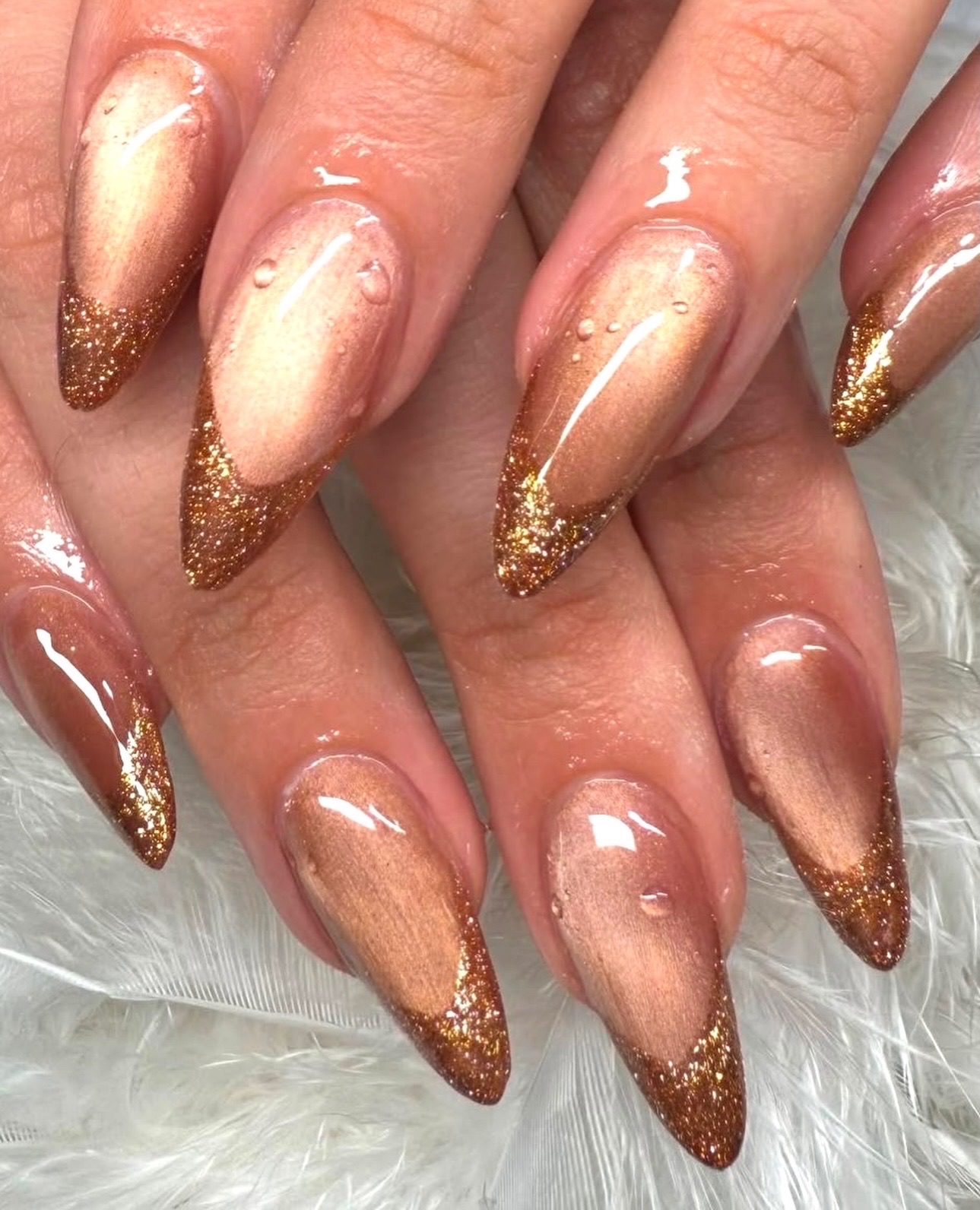 Close-up of bronze cat-eye French manicure with gold glitter tips