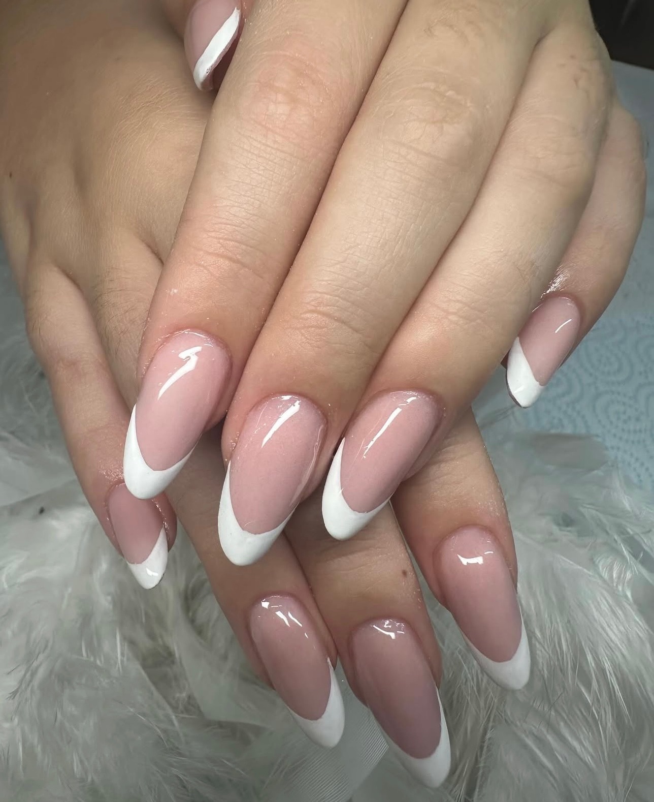 Hands with long almond-shaped French manicure on white feathers