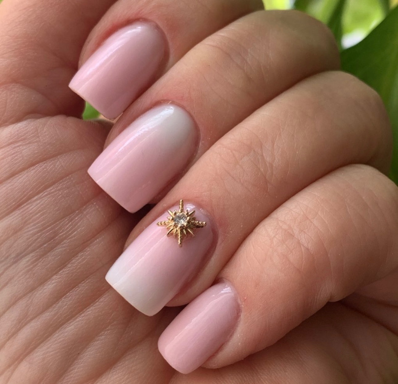 Hand with glossy pink square nails and gold star nail art